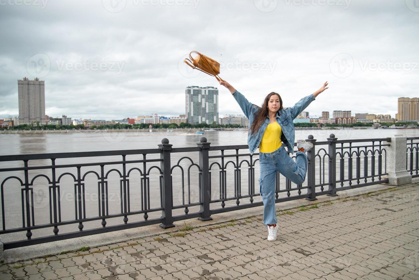 fille heureuse dans une tenue en jean sautant avec un sac à dos à la main photo