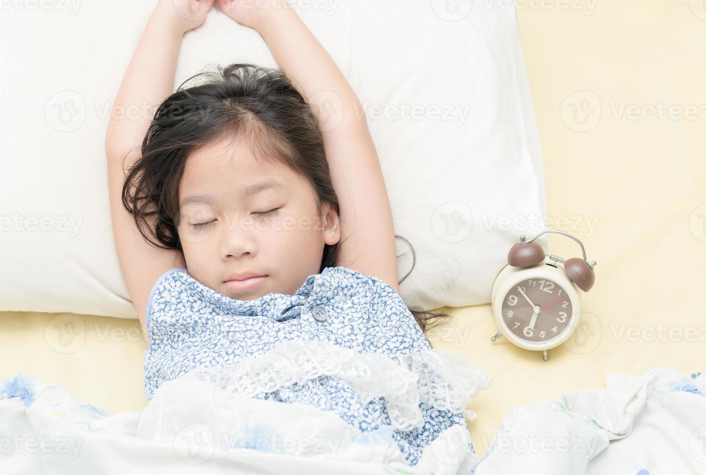 mignonne fille sommeil sur lit avec alarme horloge. photo