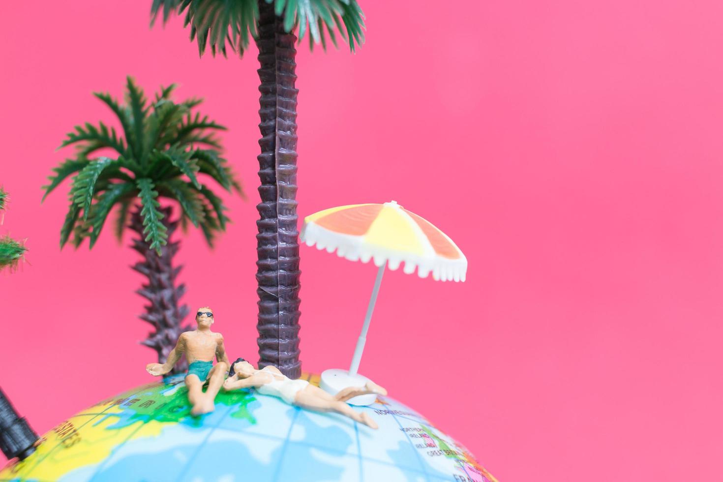 personnes miniatures portant des maillots de bain se détendre sur un globe avec un fond rose, concept de lune de miel photo