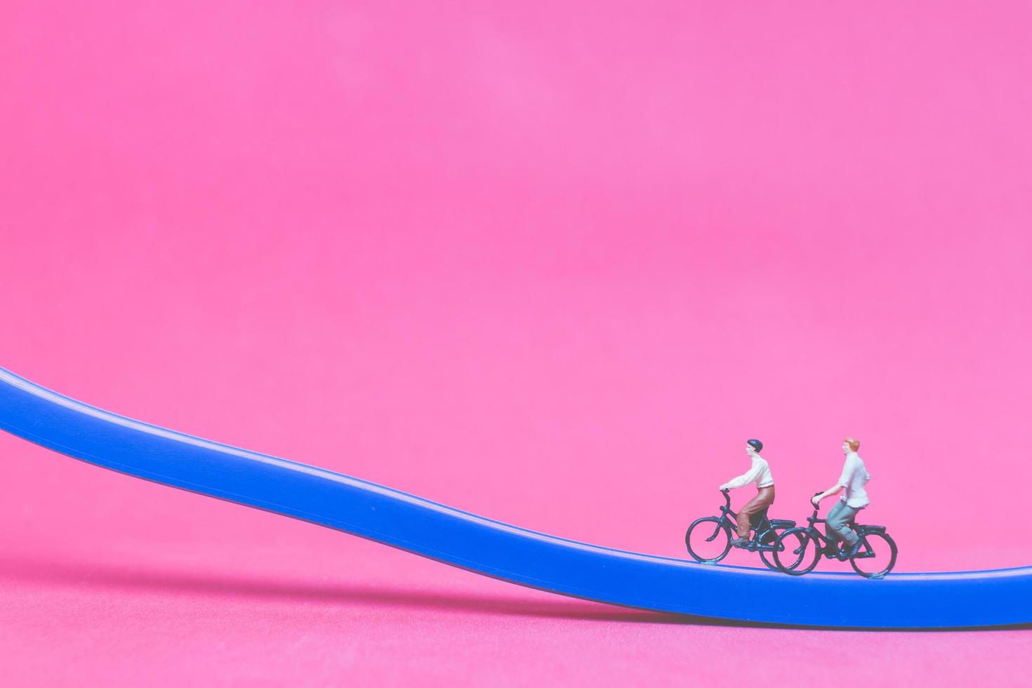 Voyageurs miniatures avec des vélos sur un pont bleu sur fond rose photo
