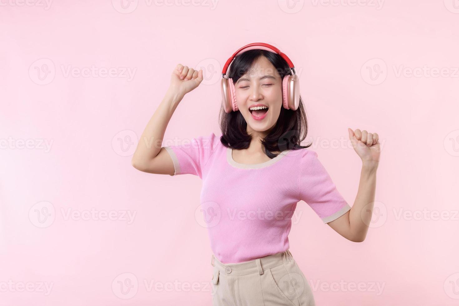 sourire jolie modèle la personne Ecoutez la musique chanson et prendre plaisir Danse avec sans fil casque de musique en ligne l'audio radio son. positif amusement sorti joyeux jeunesse femelle femme chanter sur rose isolé Contexte studio photo