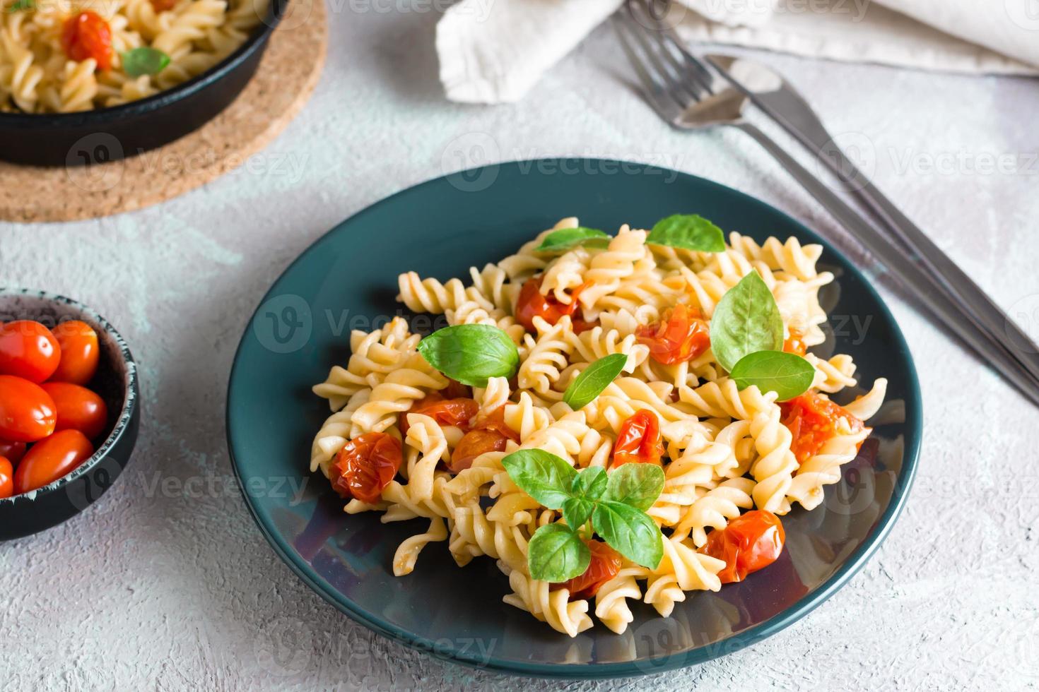 prêt à manger Pâtes avec tomates et basilic sur une assiette et Ingrédients sur le tableau. méditerranéen cuisine. fermer photo