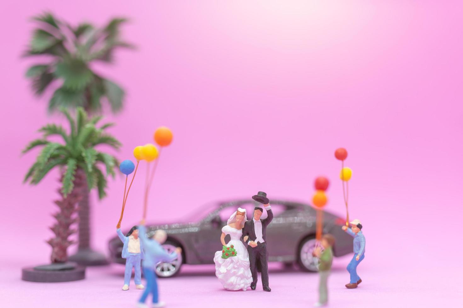 Couple miniature et famille avec des ballons colorés célébrant sur fond rose, concept de mariage photo