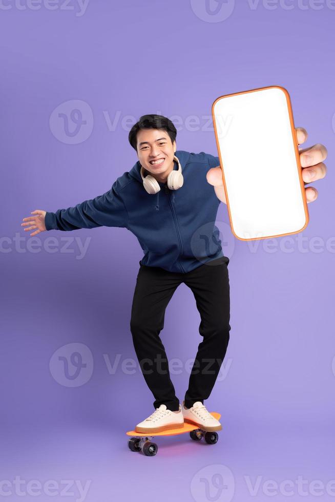 image de Jeune asiatique homme en jouant planche à roulette sur violet Contexte photo