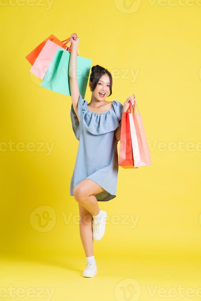 image de une magnifique asiatique fille dans une robe en portant une achats sac dans sa main posant sur une Jaune Contexte photo