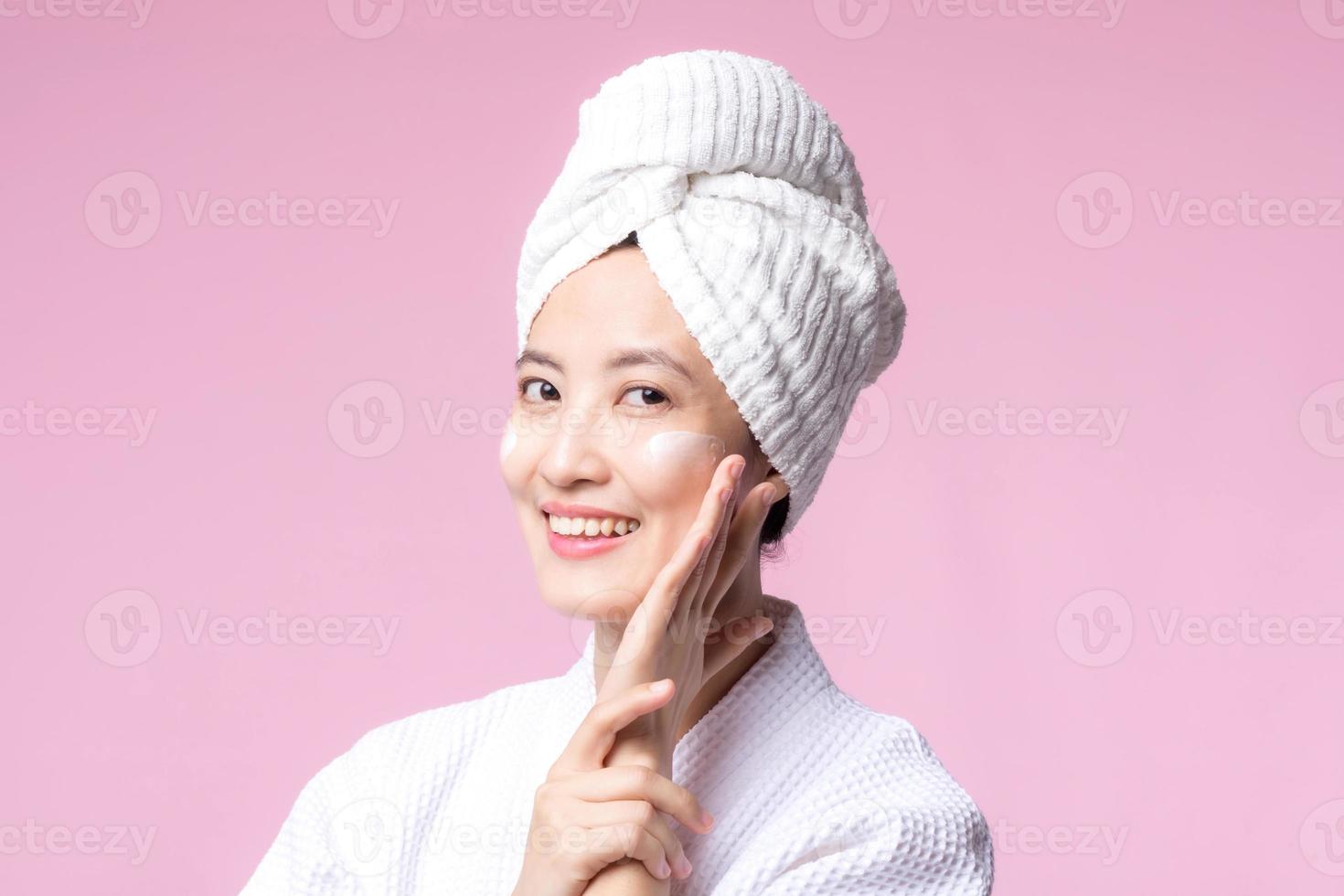 Jeune asiatique femme appliquant faciale soin de la peau visage crème, cosmétique Crème hydratante sur en bonne santé Naturel peau faire en haut affronter. portrait embrasé sourire fille la personne modèle avec se soucier beauté produit, spa, cosmétologie. photo