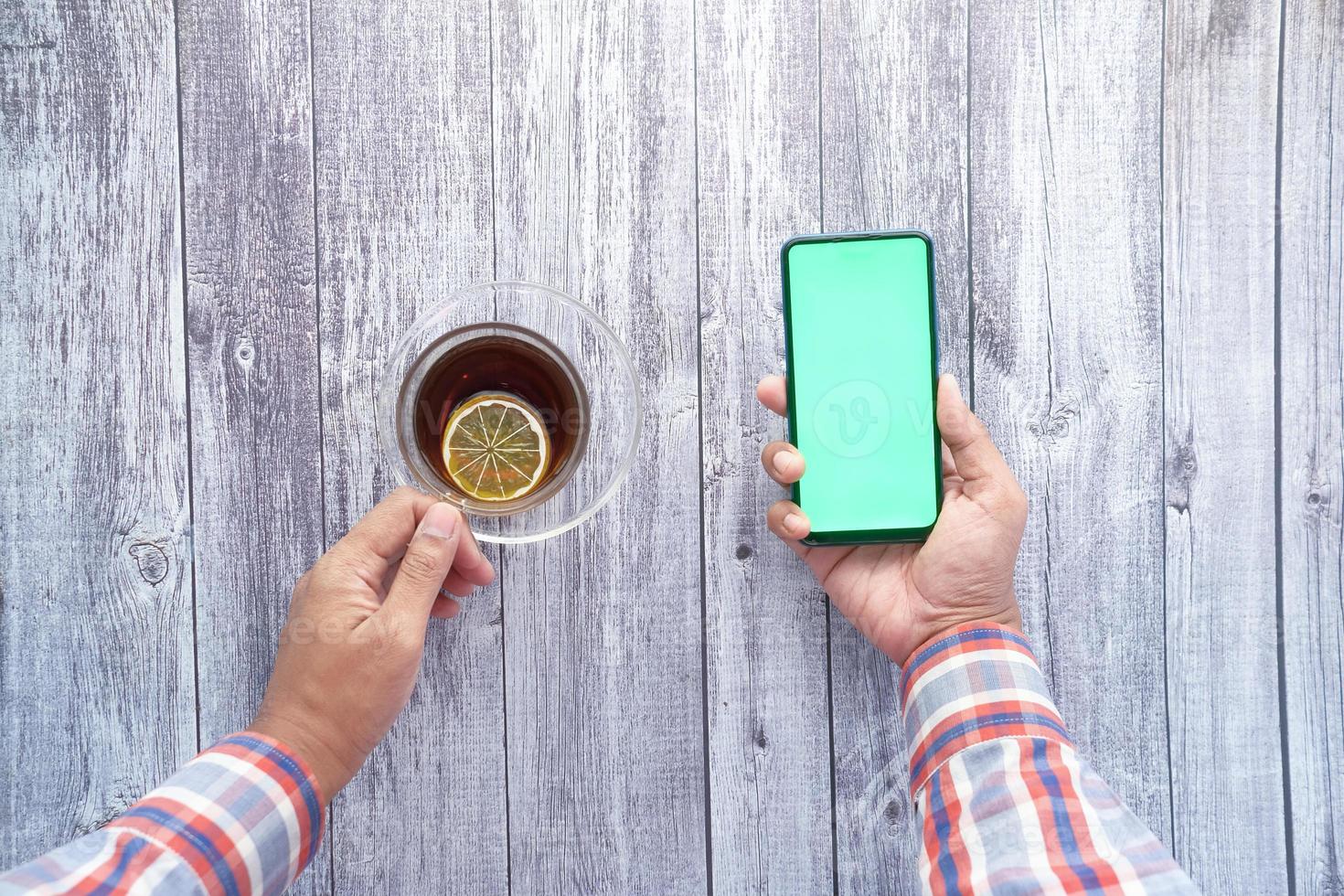 Vue de dessus de la main du jeune homme à l'aide de téléphone intelligent et de boire du thé photo