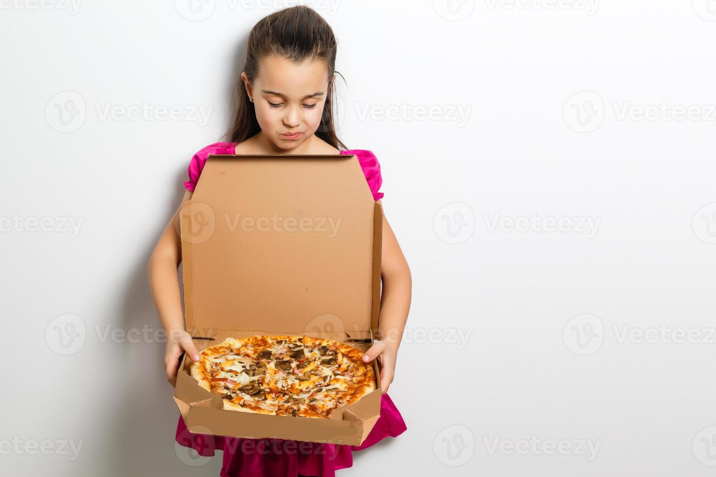 mignonne peu Indien asiatique fille enfant en mangeant savoureux Pizza dans boîte. permanent isolé plus de blanc Contexte. photo