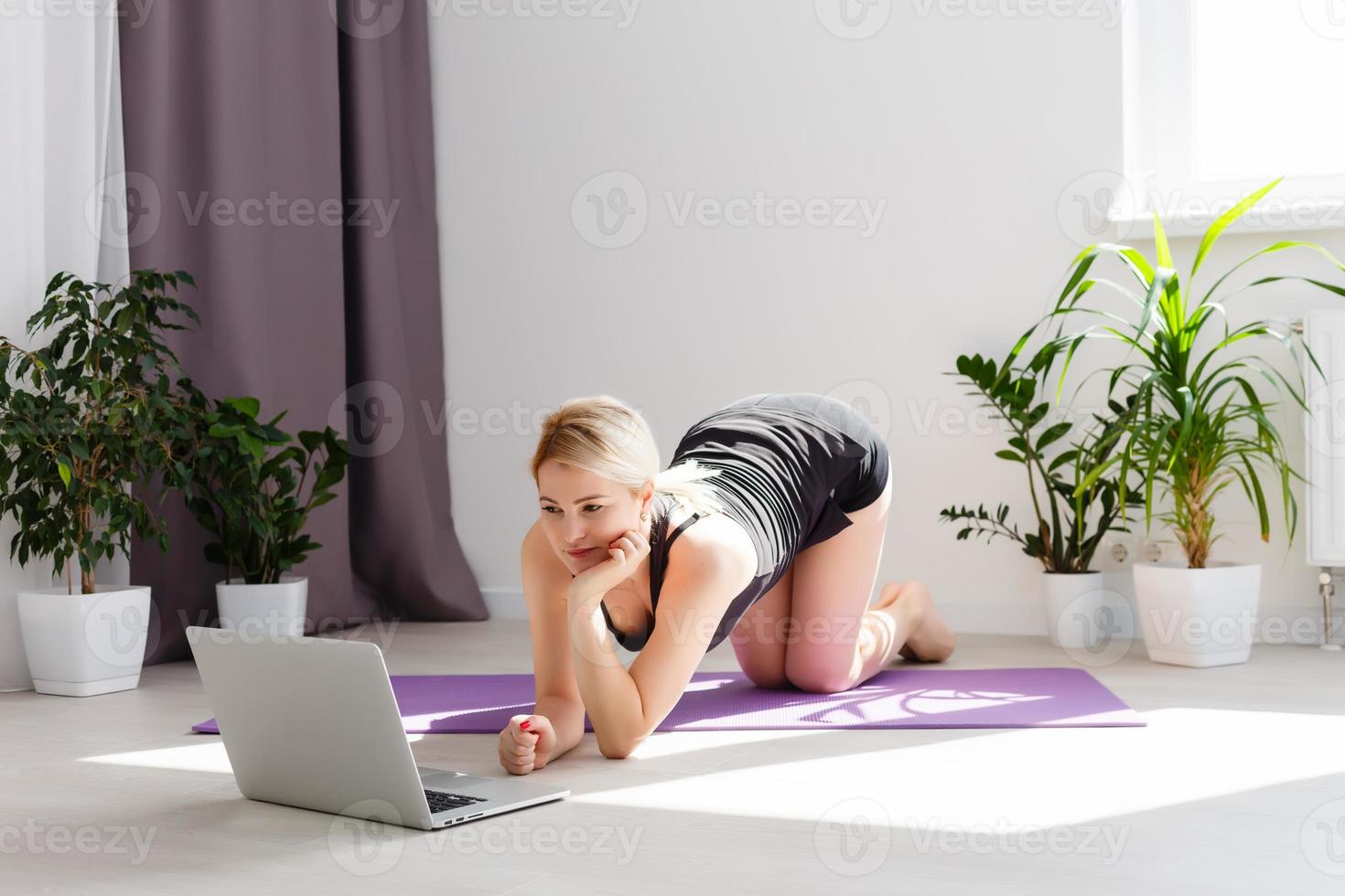 seul fille Faire yoga des exercices en ligne sur portable sur le sol dans le lumière chambre, rester Accueil sûr monde. photo
