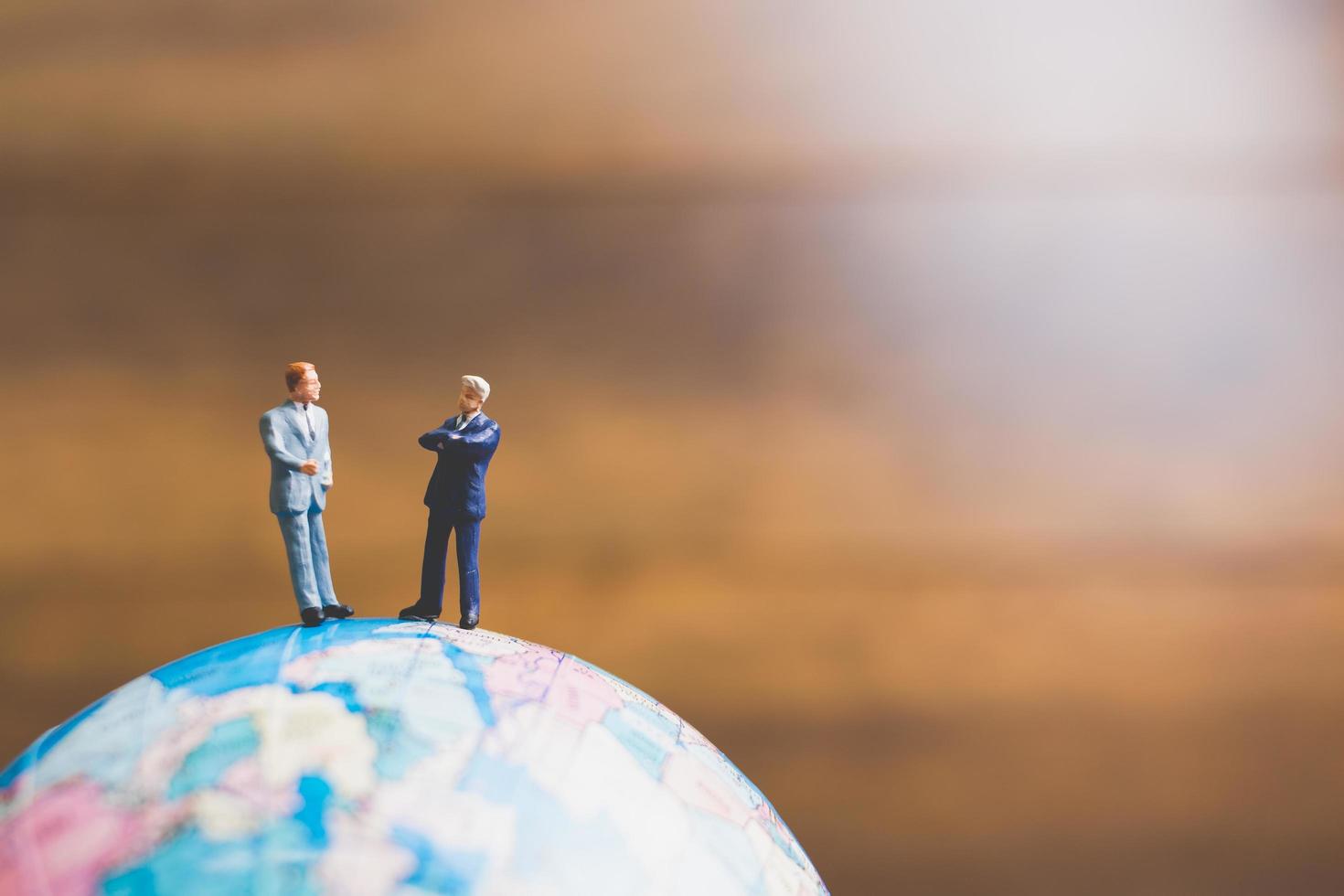 Hommes d'affaires miniatures debout sur une carte du monde globe avec un fond brun photo