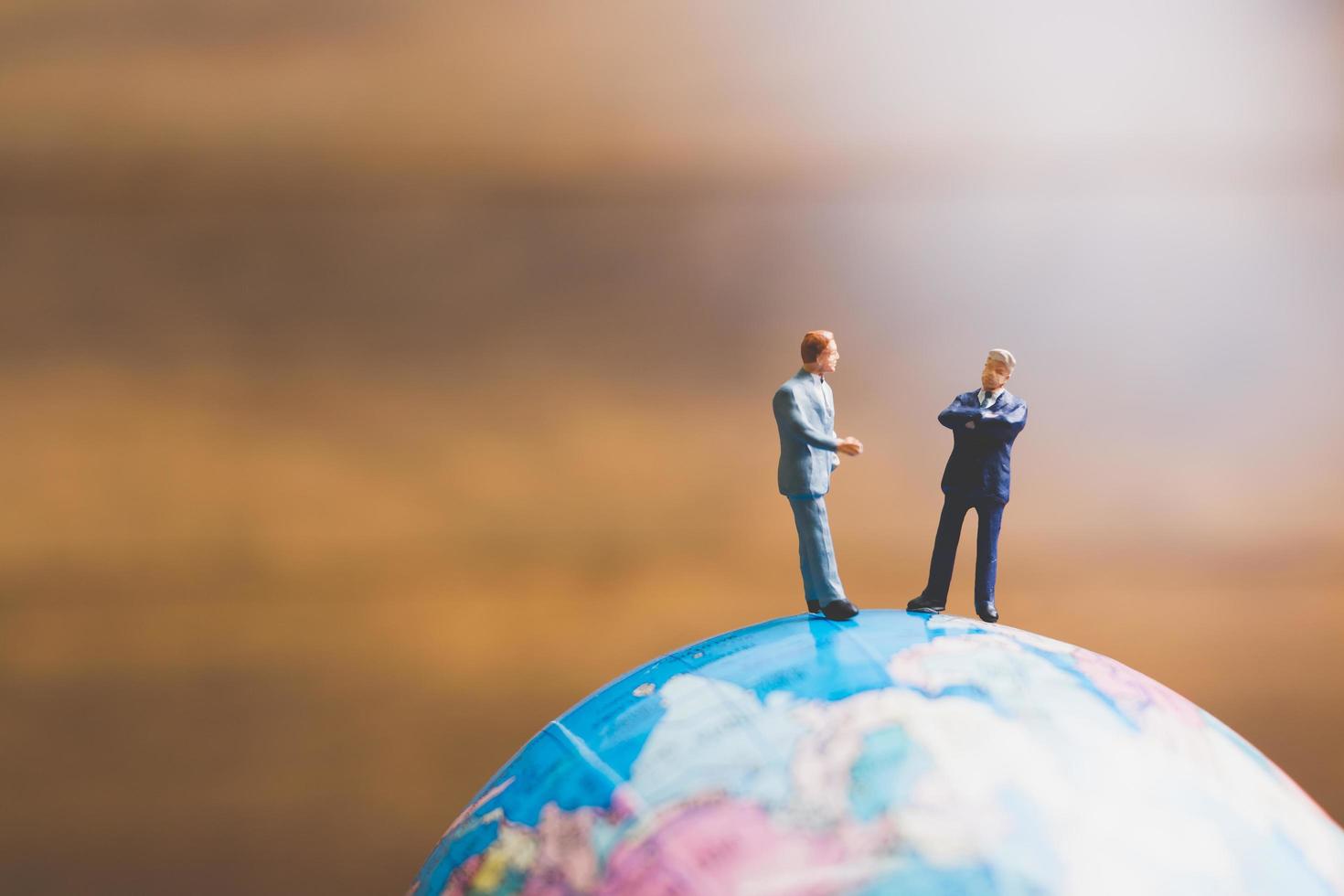 Hommes d'affaires miniatures debout sur une carte du monde globe avec un fond brun photo