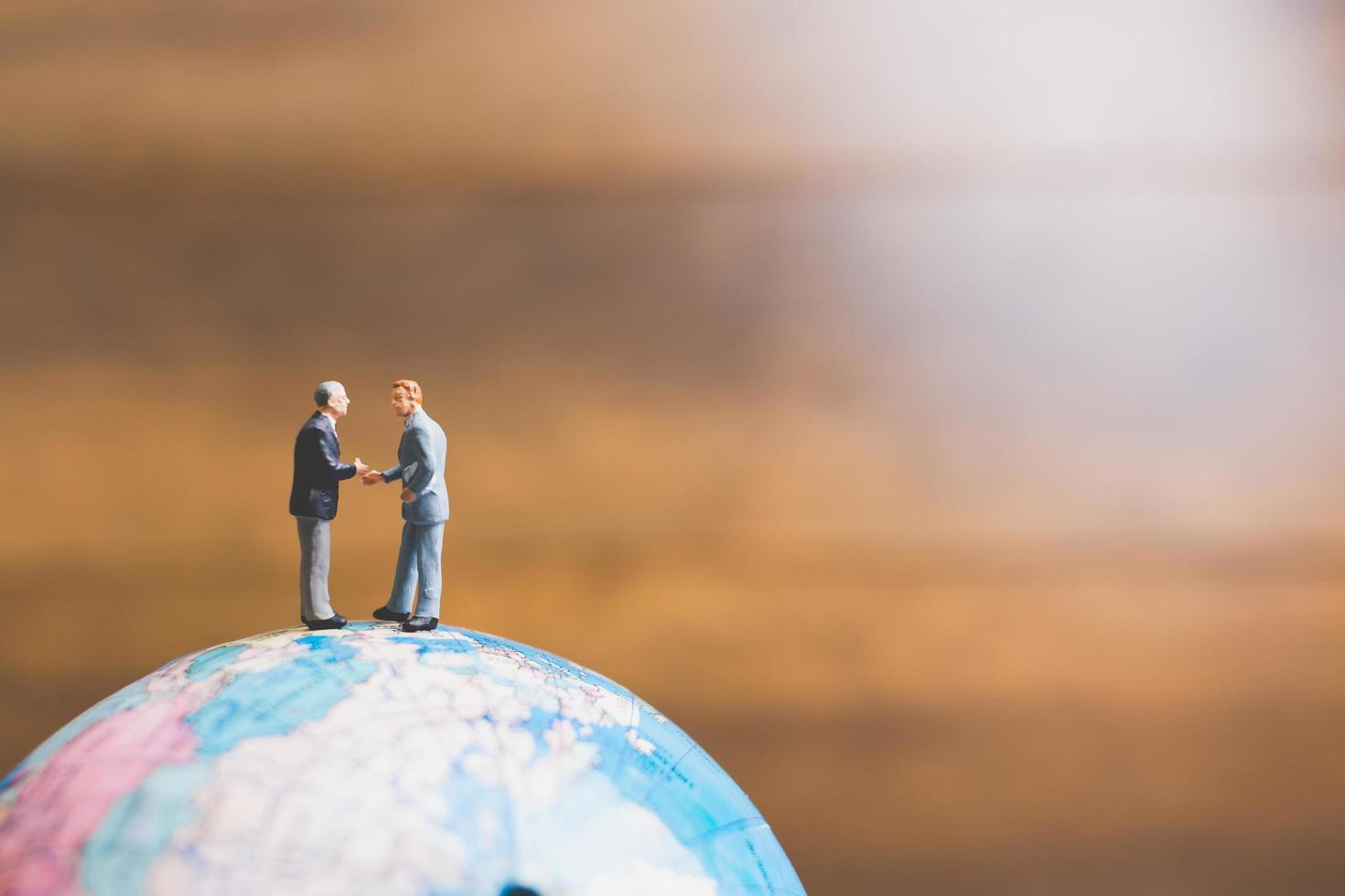 Hommes d'affaires miniatures debout sur une carte du monde globe avec un fond brun photo