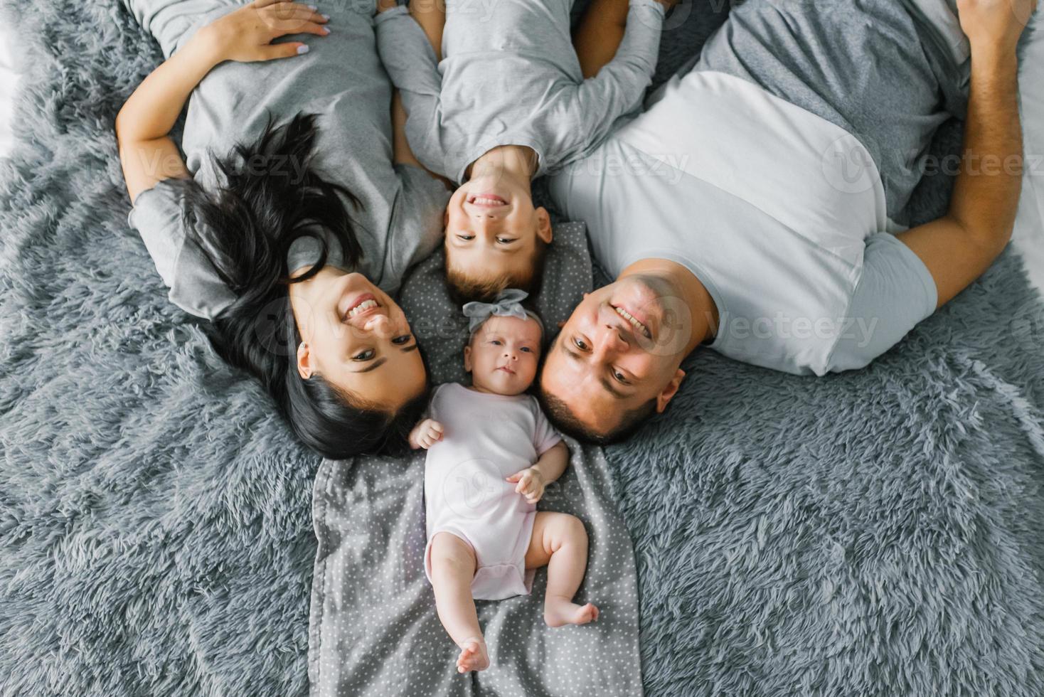 content famille avec deux petit les enfants sont mensonge repos sur le lit et souriant. Haut vue photo