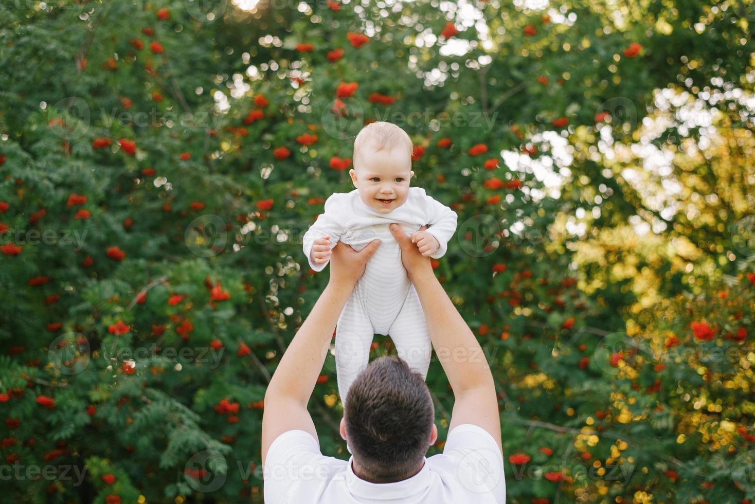 une père pièces avec le sien fils dans le parc dans le été. une homme détient une peu garçon en haut dans le sien bras photo