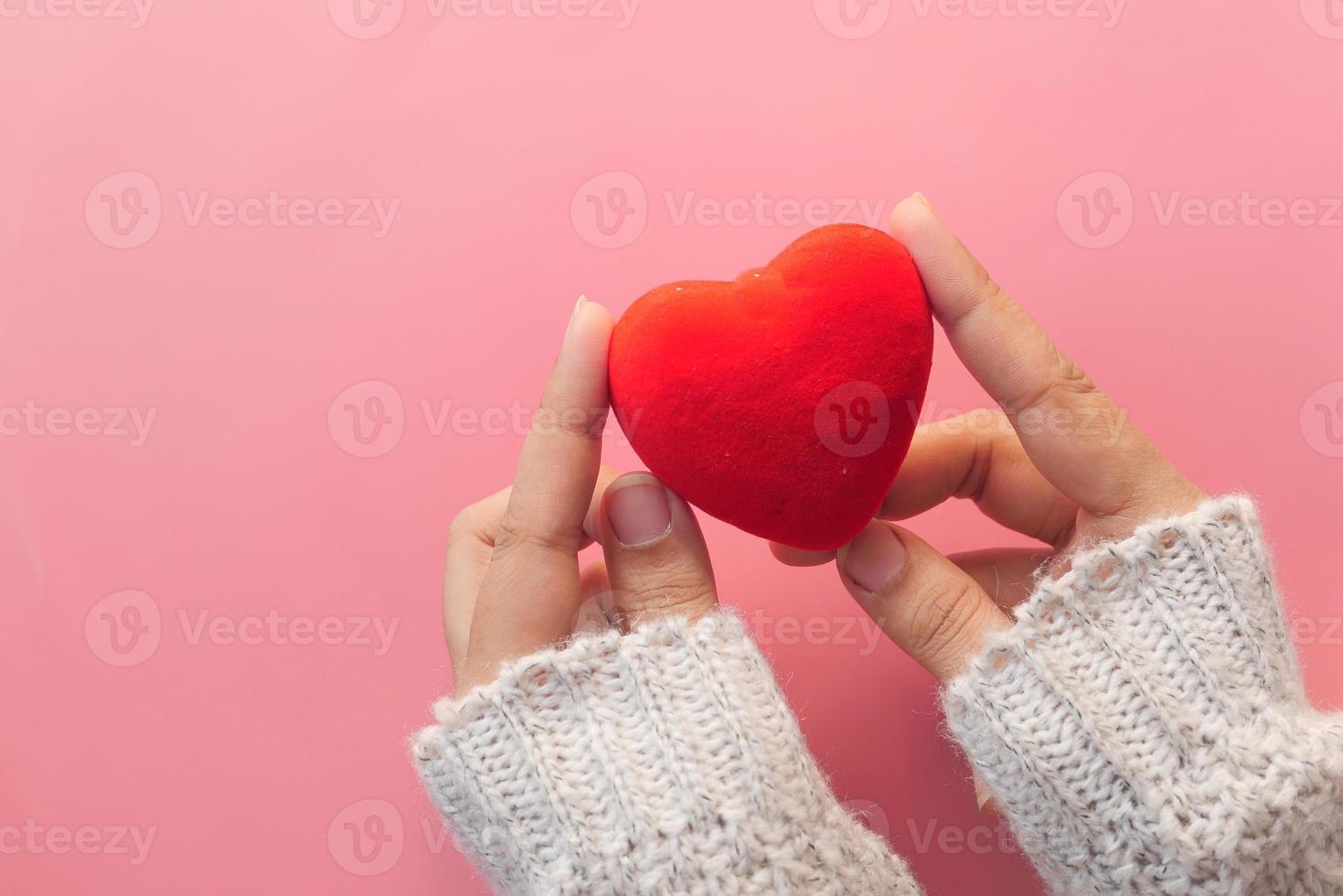 main de femme tenant un coeur rouge sur fond rose photo