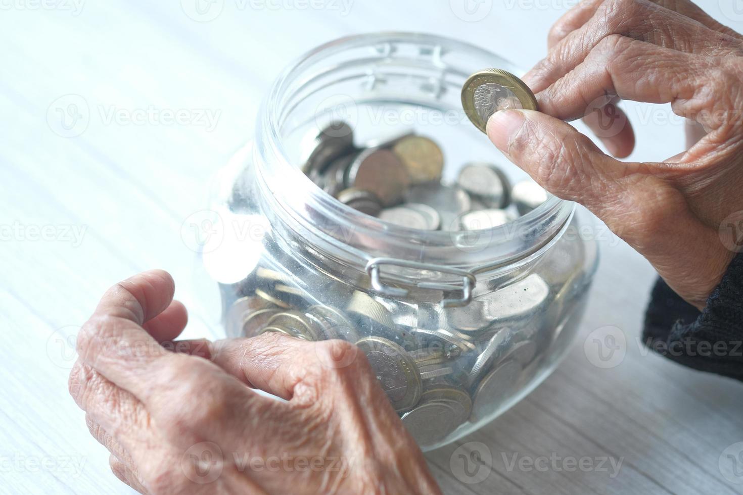 Close up of senior woman's hand économiser des pièces dans un pot photo