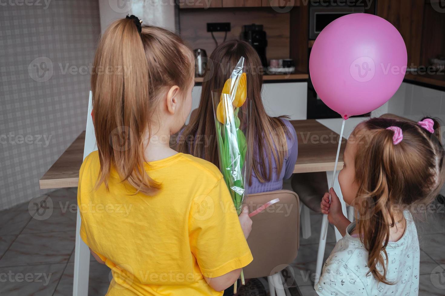 filles féliciter leur maman sur de la mère jour, une carte avec une cœur, fleurs et une ballon à Accueil dans le cuisine. les enfants surprise leur mère pour le vacances. photo