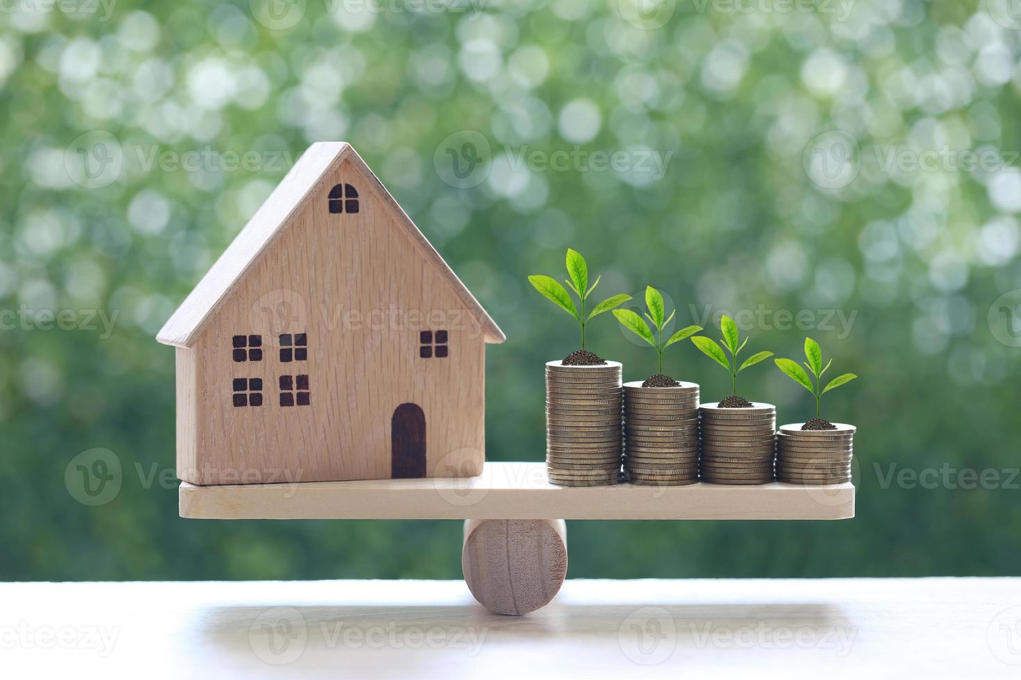 Maison modèle avec des plantes poussant sur une pile de pièces de monnaie sur une balançoire à l'échelle du bois avec un fond vert naturel, l'investissement des entreprises et le concept immobilier photo