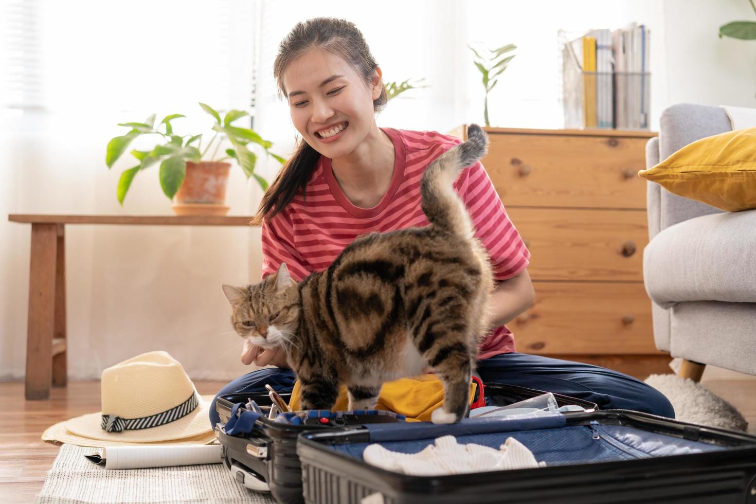 randonneur Voyage de voyage, asiatique Jeune femme en jouant avec sa chat, animal de compagnie tandis que vérifier liste, emballage ou préparer vêtements dans bagage, Voyage Cas pour périple voyage. voyage de voyageur, vacances vacances. photo