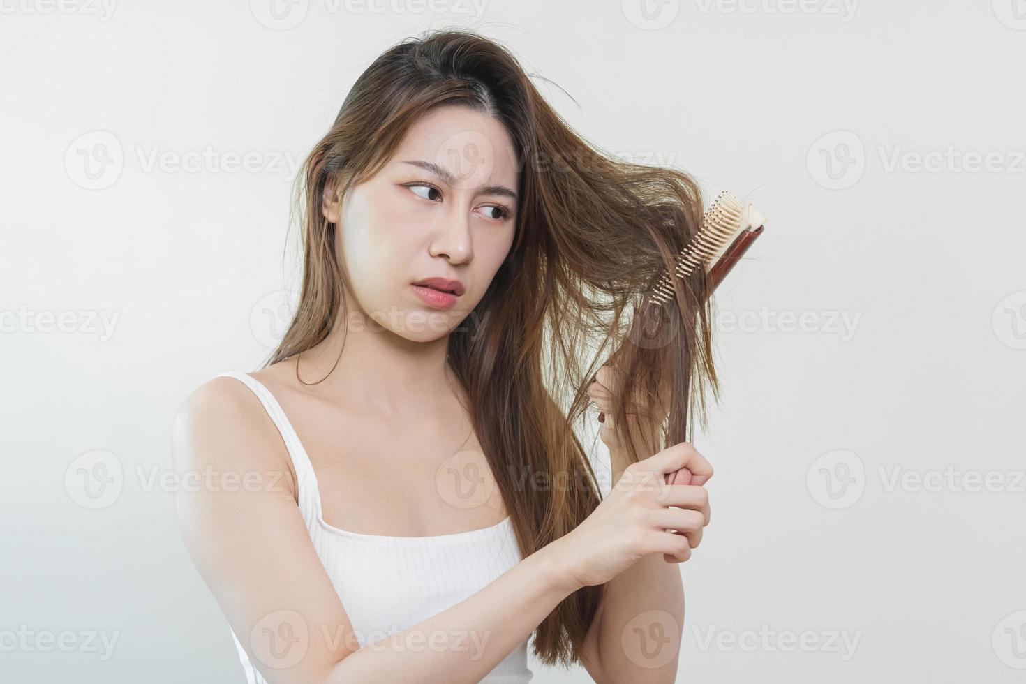 endommagé cheveux, frustré asiatique Jeune femme, fille main dans en portant brosse scission prend fin désordonné tandis que ratissage cheveux, non brossé sec longue cheveux. santé se soucier beauté, portrait isolé sur blanc Contexte. photo