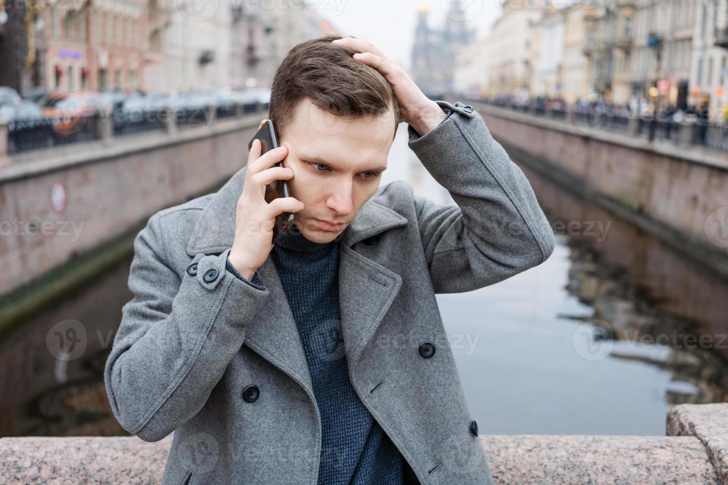 Beau Jeune homme en utilisant mobile téléphone, portant un élégant gris manteau, des stands photo