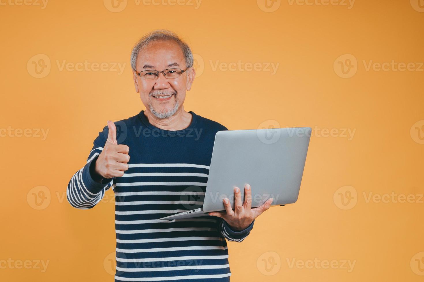 asiatique Sénior homme en utilisant portable ordinateur pour travail après retraite sur le Jaune Contexte. photo