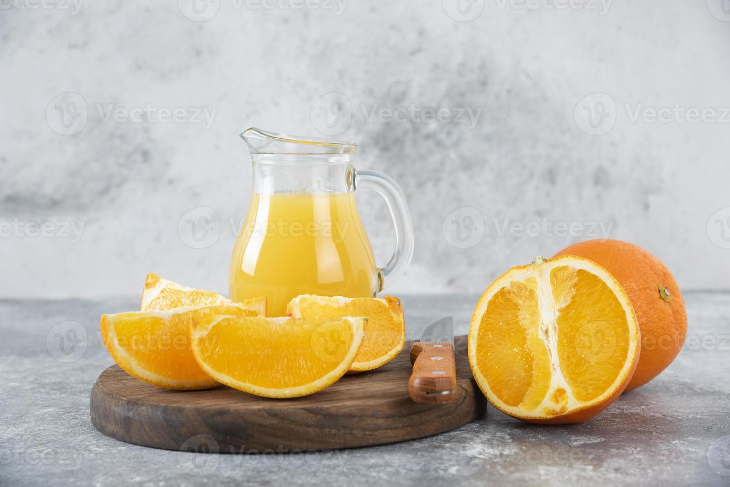 Tranches d'orange avec un pichet en verre de jus de fruits frais placé sur une planche ronde en bois photo