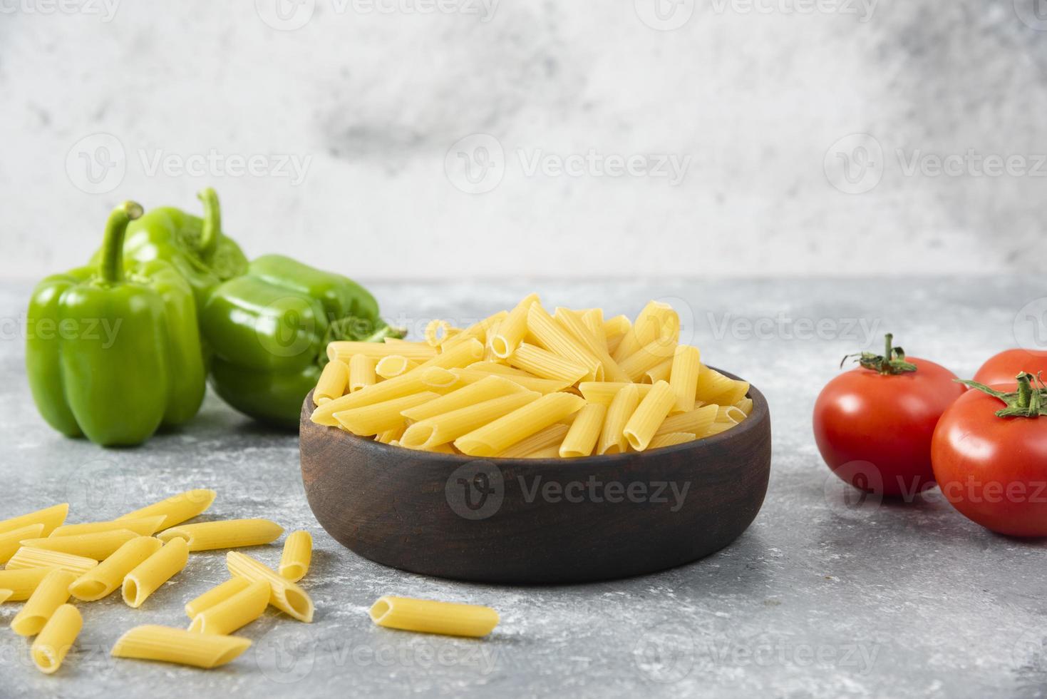 Pâtes non cuites avec des légumes frais et mûrs placés sur une table en pierre photo