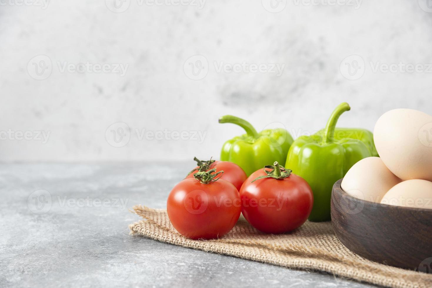 Bol en bois plein d'oeufs de poule crus avec des légumes frais et mûrs sur un sac photo