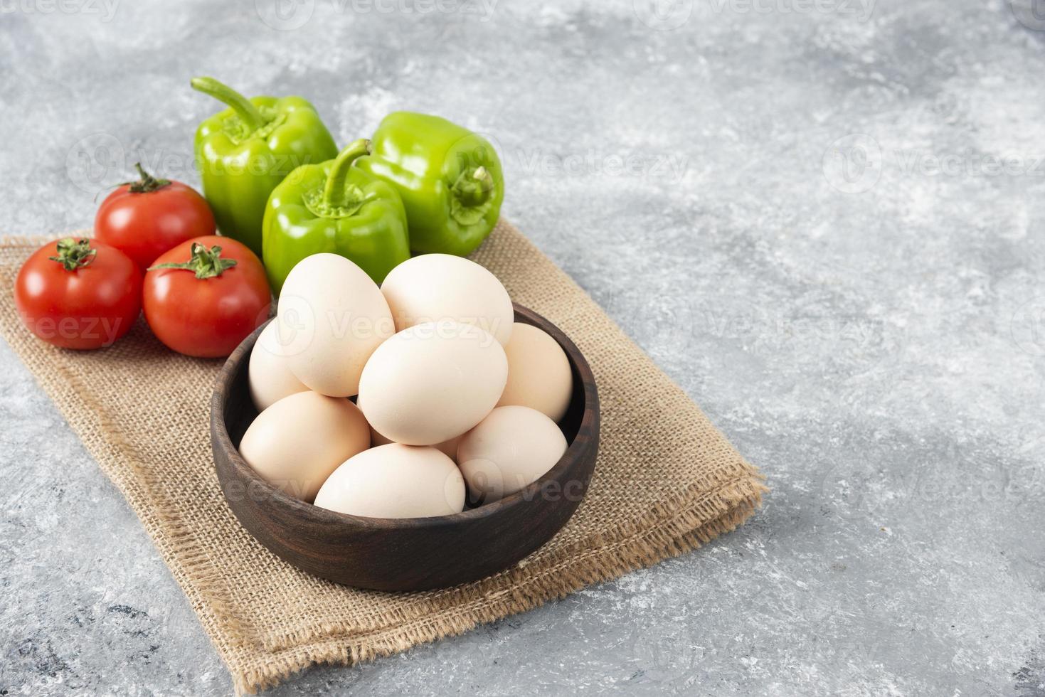 Bol en bois plein d'oeufs de poule crus avec des légumes frais et mûrs sur un sac photo