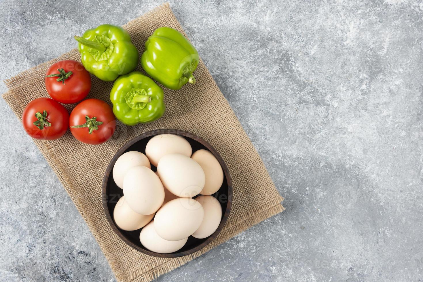 Bol en bois plein d'oeufs de poule crus avec des légumes frais et mûrs sur un sac photo