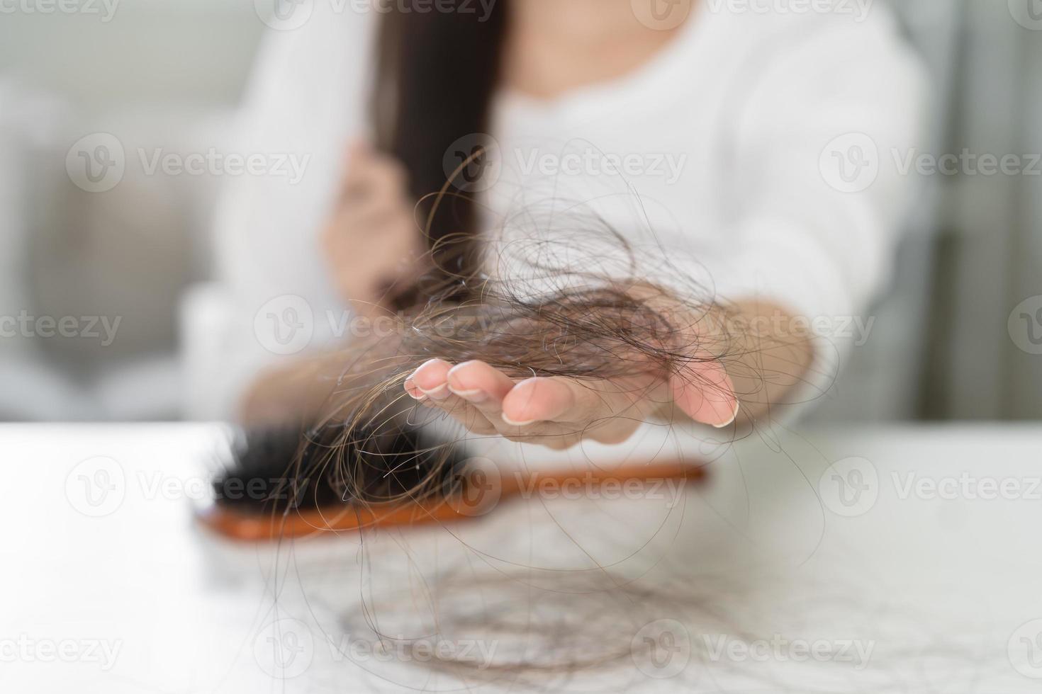 sérieux, inquiet asiatique Jeune femme, fille en portant brosse, spectacle sa peigne, brosse à cheveux avec longue perte cheveux problème après brossage, cheveux tomber en dehors sur sa main dans vivant chambre. santé se soucier, beauté traitement. photo