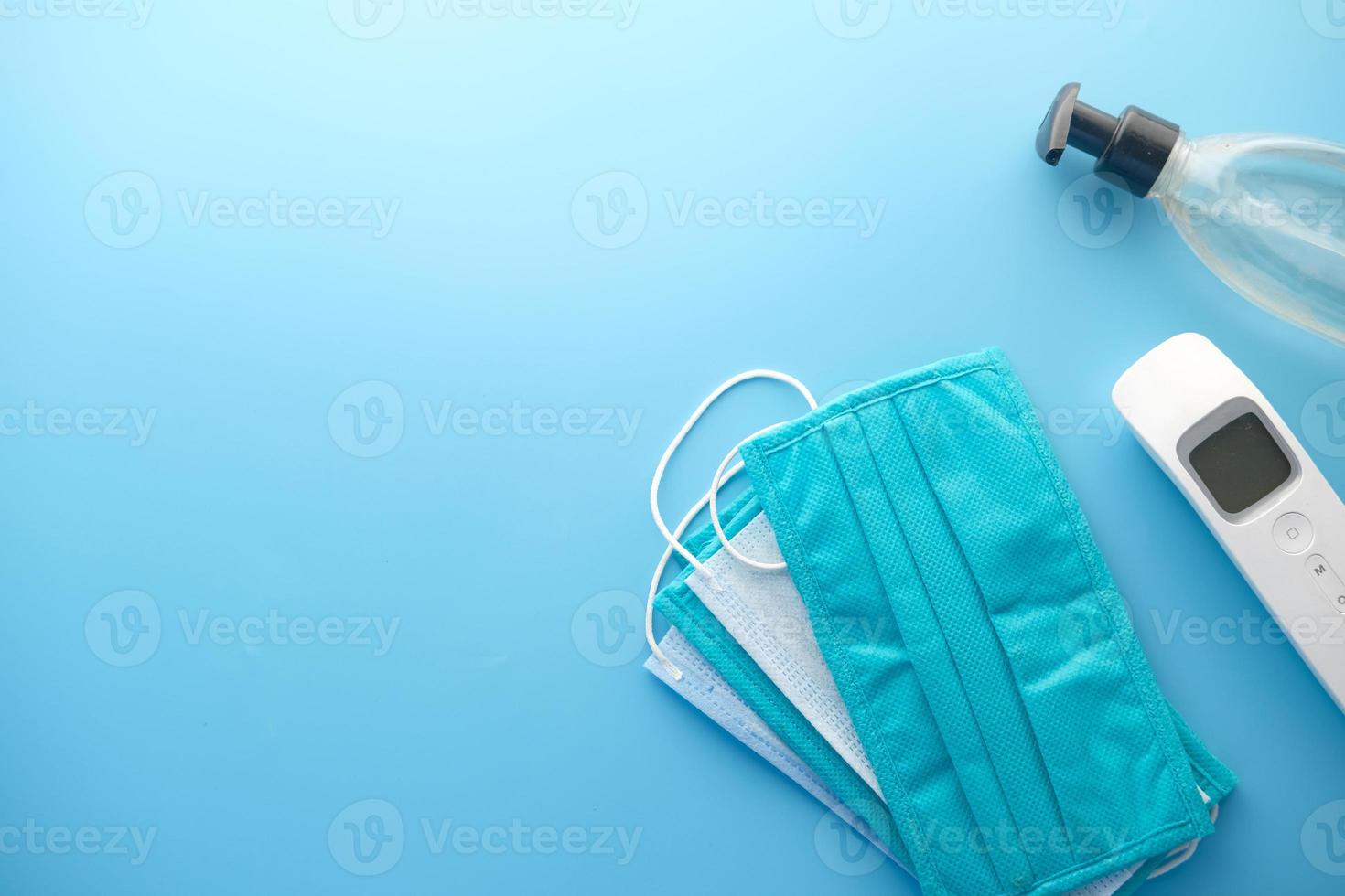 masques chirurgicaux, thermomètre et désinfectant pour les mains sur fond bleu photo