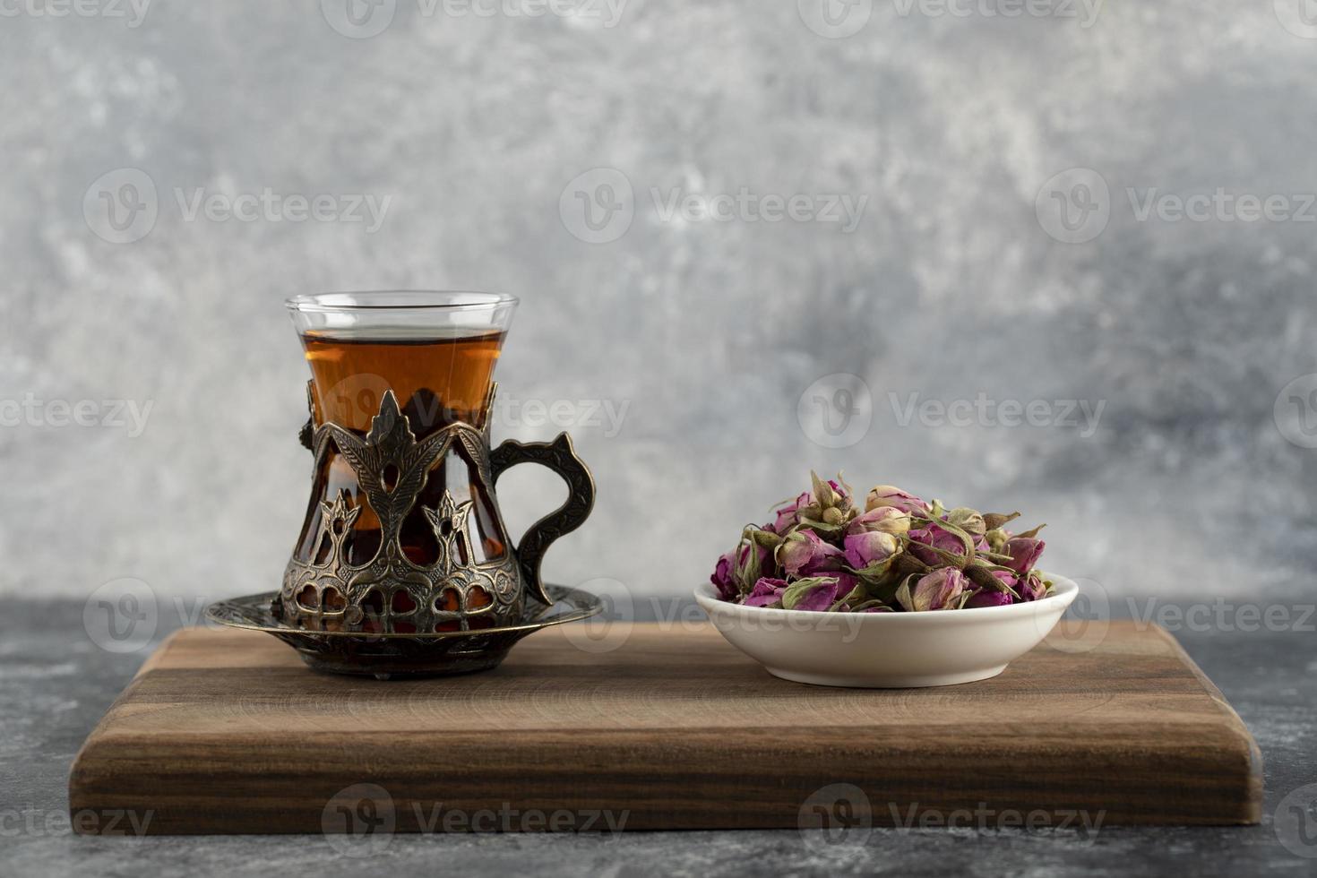Une tasse en verre de thé chaud avec des roses séchées sur une planche à découper en bois photo