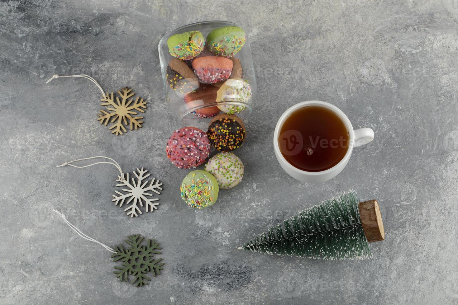 beignets sucrés colorés avec un jouet d'arbre de Noël et une tasse de thé chaud photo