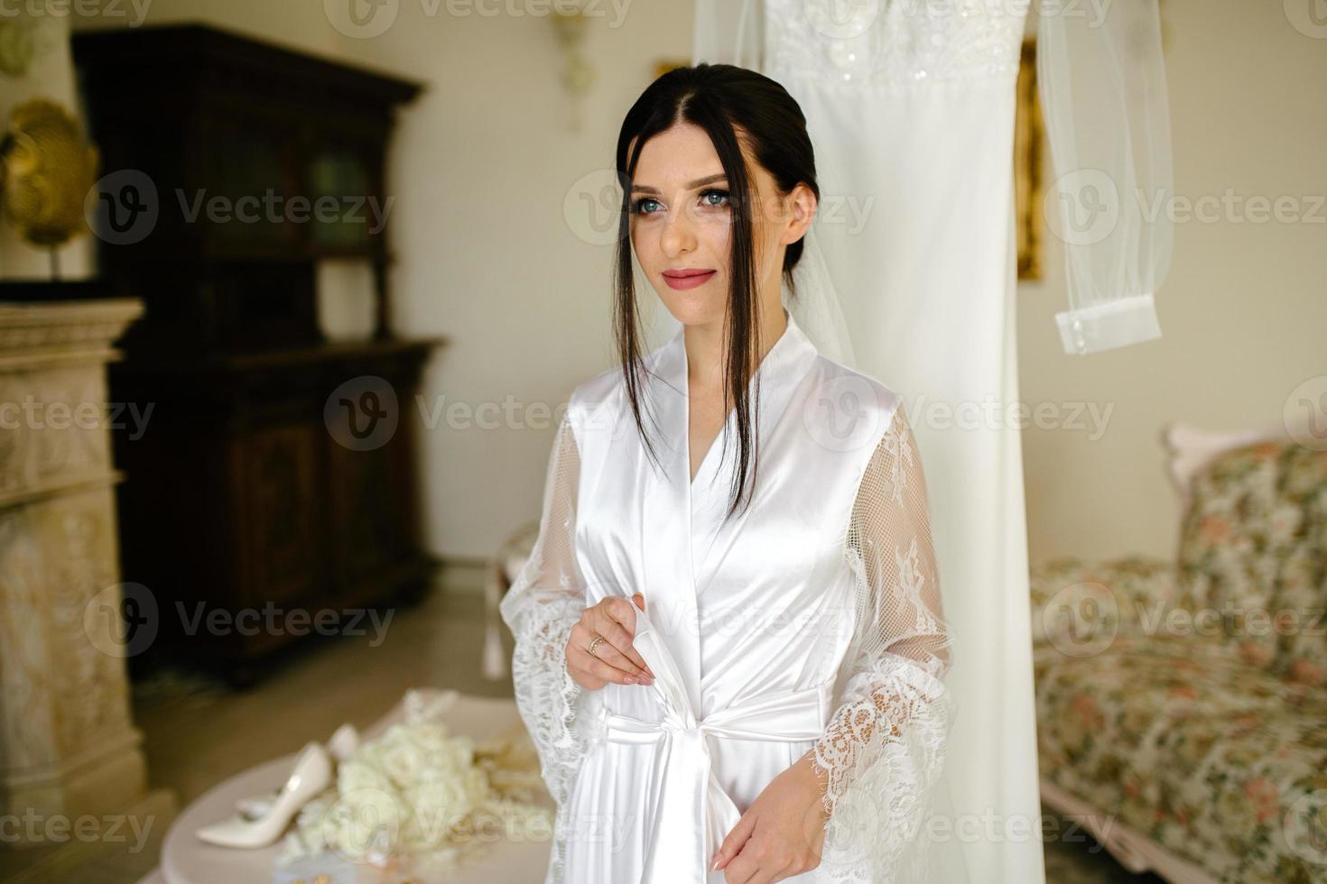 romantique atmosphère de le de la mariée Matin. la mariée dans une maison. la mariée Matin préparation. la mariée dans magnifique robe près le mannequin avec robe à l'intérieur à maison. prendre plaisir chaque moment. photo
