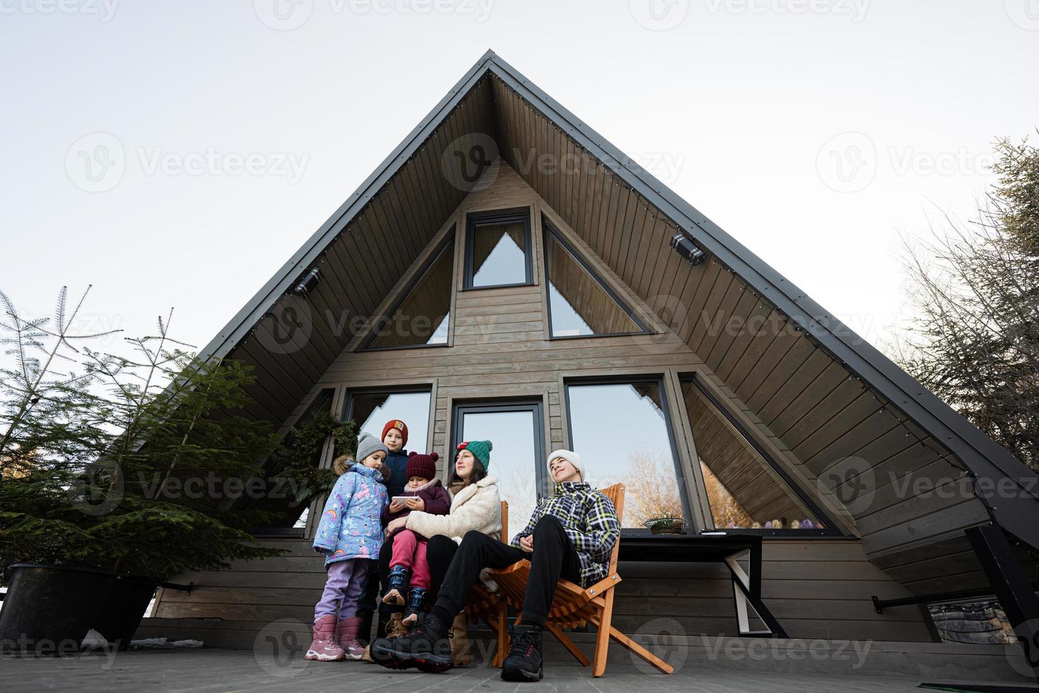 mère avec quatre les enfants asseoir sur terrasse de la grille minuscule maison dans le montagnes. photo