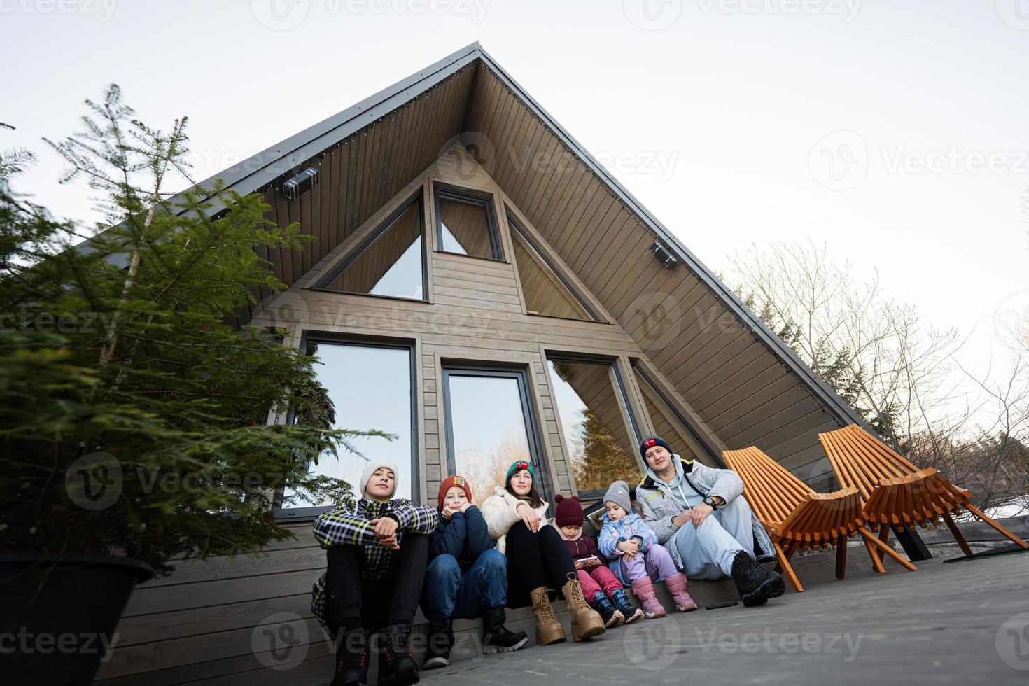 grand famille avec quatre les enfants asseoir sur terrasse de la grille minuscule maison dans le montagnes. photo