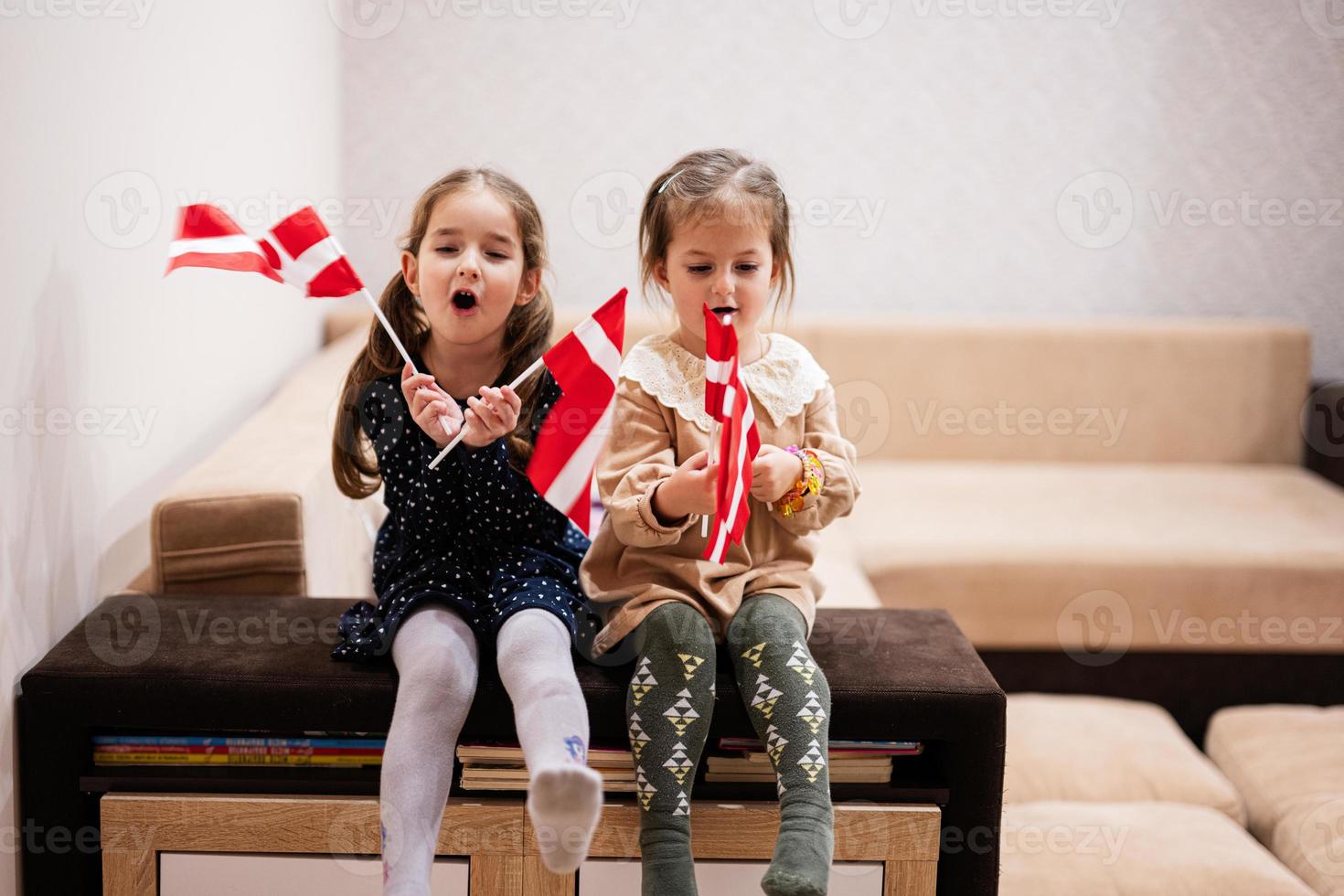 deux sœurs sont assises sur un canapé à la maison avec des drapeaux danois sur les mains. Danemark enfants filles avec drapeau. photo