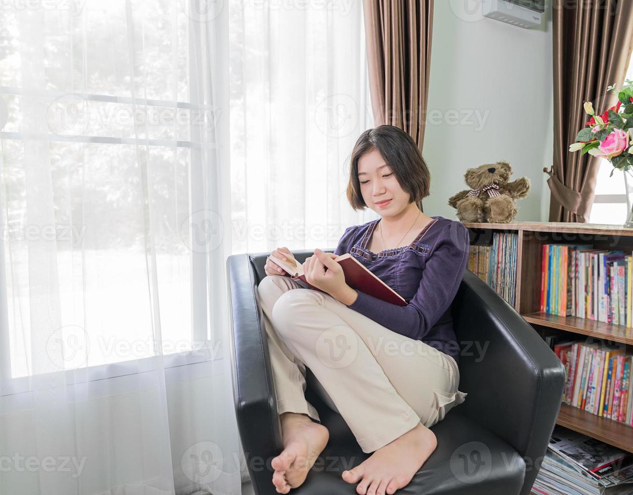 jeune femme asiatique cheveux courts lire un livre dans le salon photo