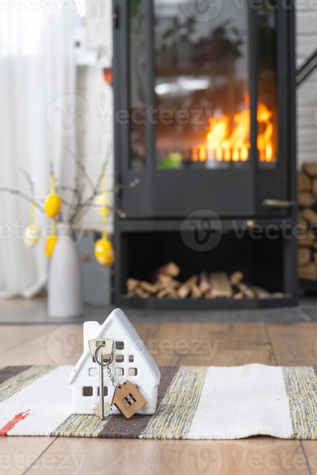 clé à maison près cheminée le fourneau avec Feu et bois de chauffage. confortable Accueil foyer avec Pâques décor, coloré des œufs dans une panier et lapin. bâtiment, en mouvement, hypothèque, location et achat réel domaine, Assurance photo