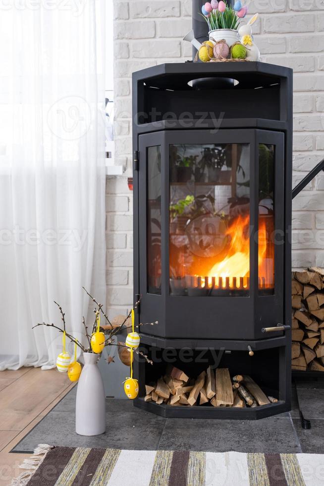 Pâques décor près cheminée le fourneau avec Feu et bois de chauffage. confortable Accueil foyer dans intérieur avec mis en pot des plans, coloré Pâques œufs, Pâques lapin et bouquet. printemps dans une pays maison photo