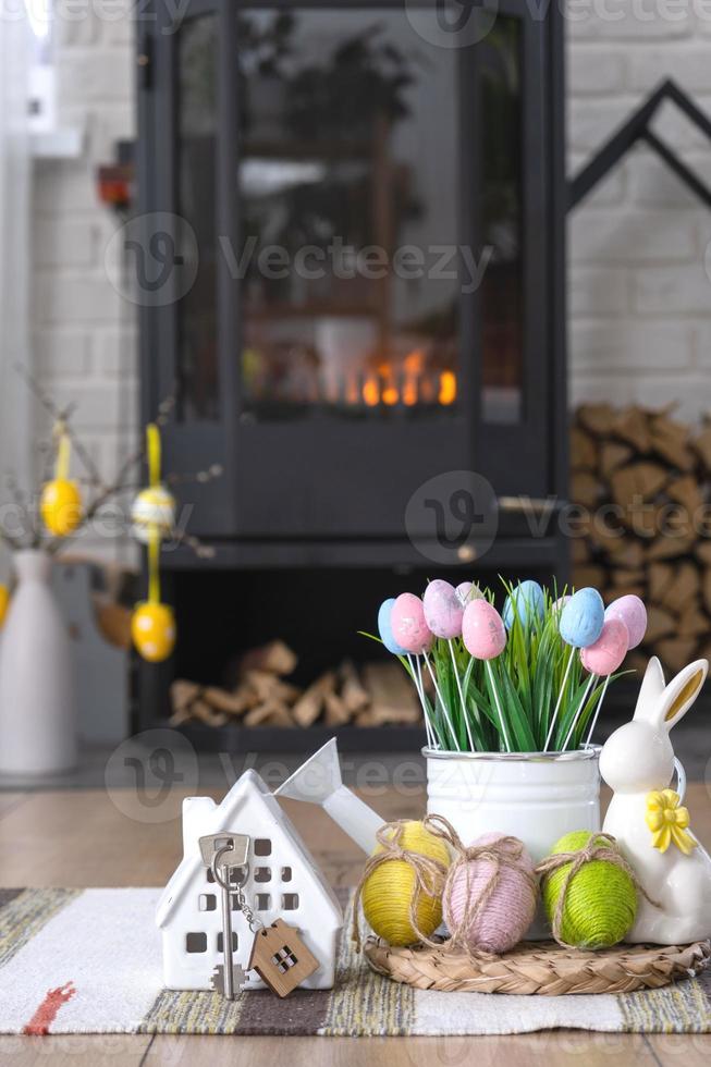 clé à maison près cheminée le fourneau avec Feu et bois de chauffage. confortable Accueil foyer avec Pâques décor, coloré des œufs dans une panier et lapin. bâtiment, en mouvement, hypothèque, location et achat réel domaine, Assurance photo