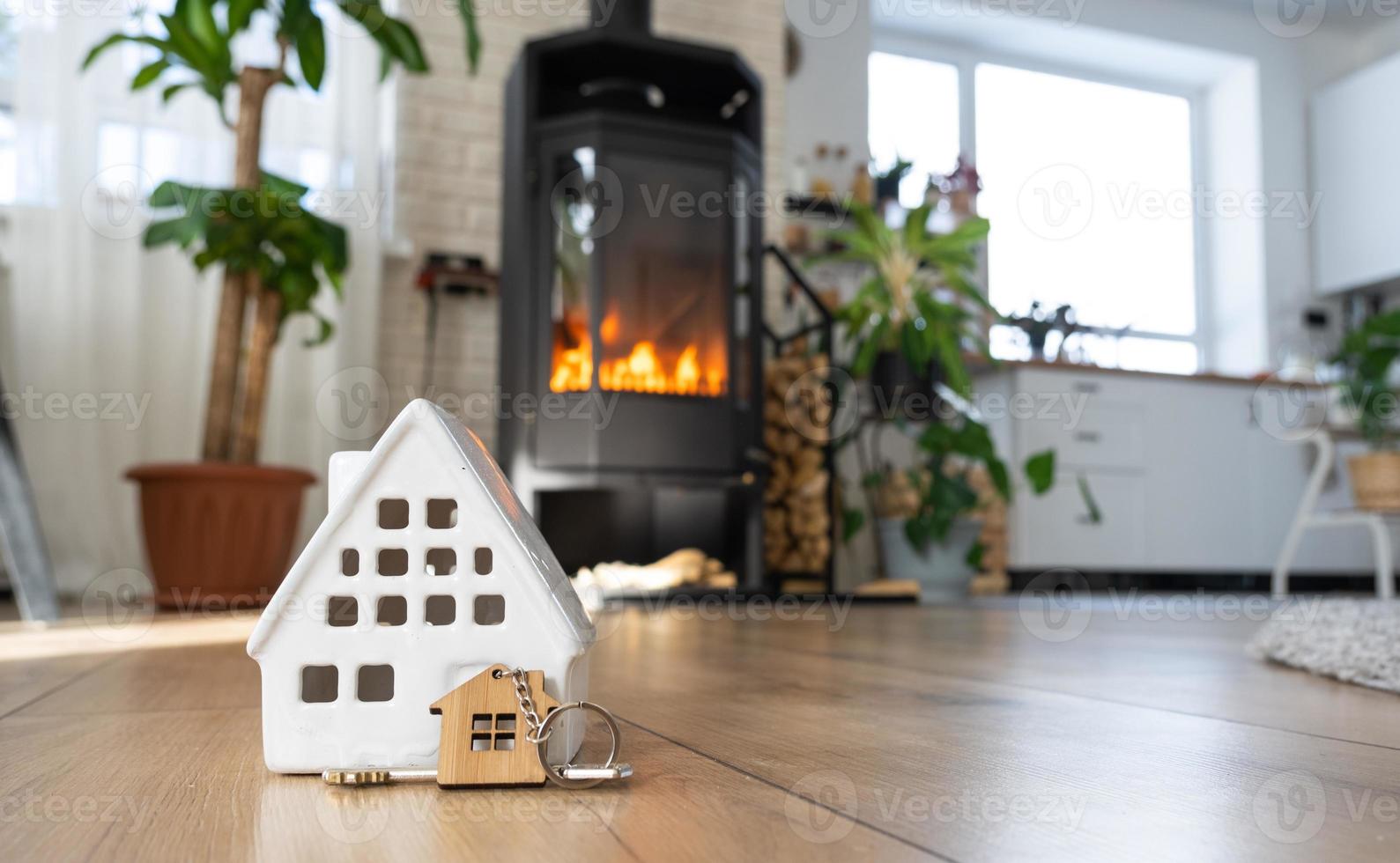 clé de la maison avec porte-clés sur fond de poêle cheminée avec feu et bois de chauffage. foyer chaleureux. construction, conception, projet, déménagement dans une nouvelle maison, hypothèque, location et achat immobilier photo