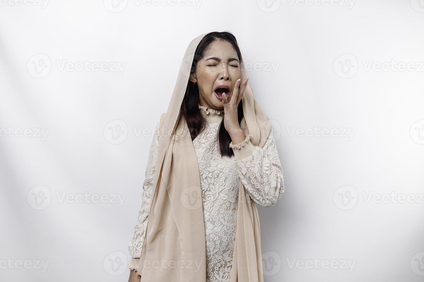 portrait de somnolent attrayant asiatique musulman femme portant une foulard, sentiment fatigué après nuit sans pour autant dormir, bâillement, couvrant ouvert bouche avec paume photo