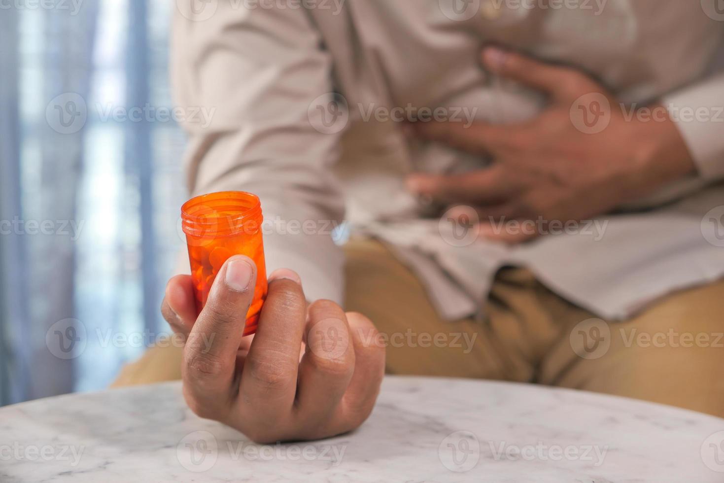 Homme souffrant de maux d'estomac tenant une bouteille de pilules orange photo