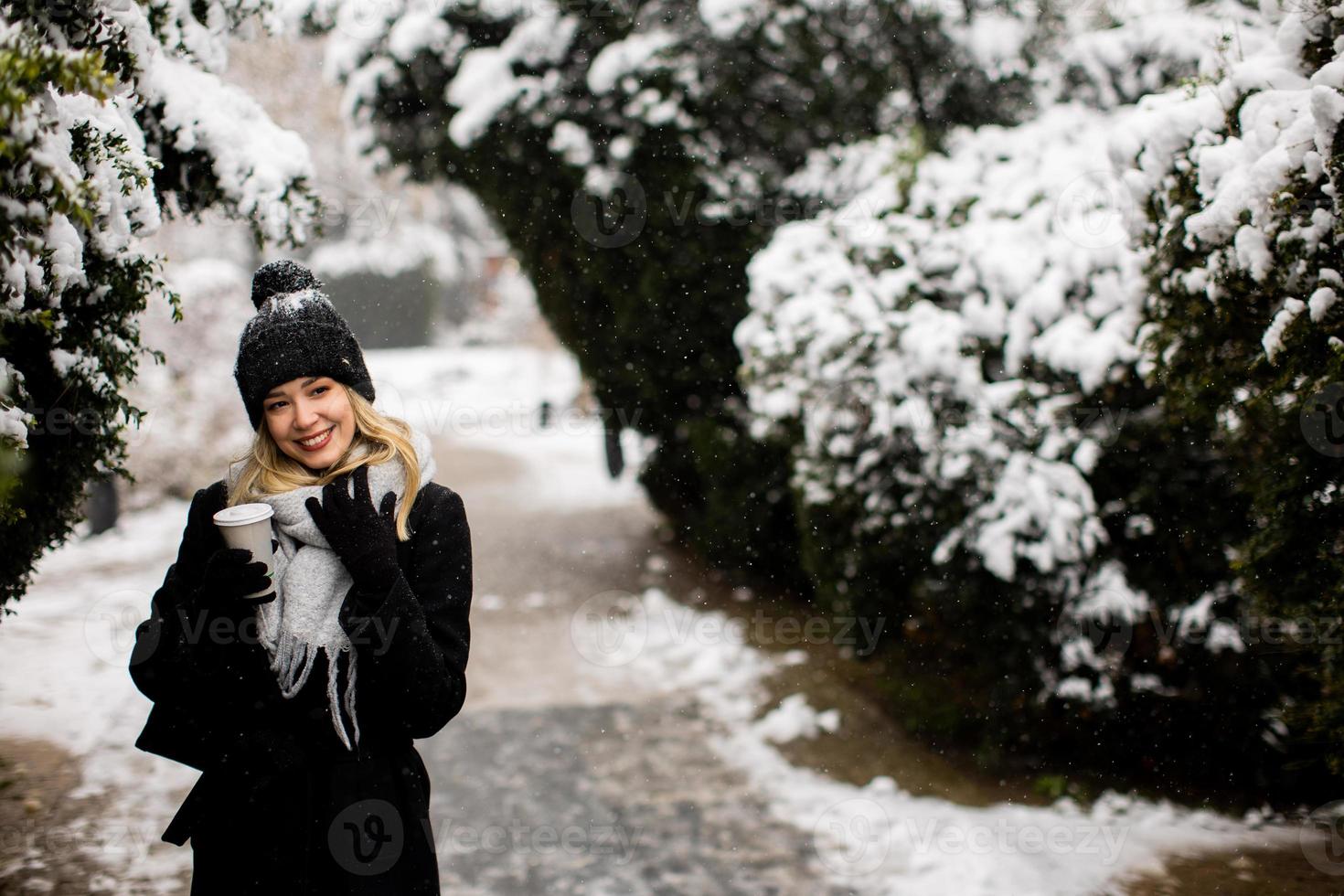 Jeune femme dans chaud vêtements profiter dans neige avec à emporter café tasse photo