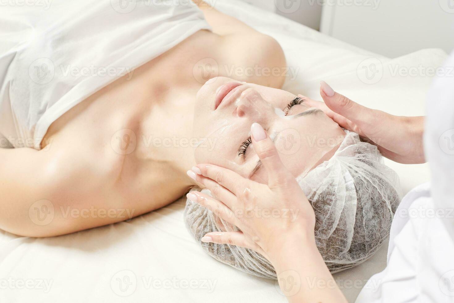 l'esthéticienne lisse le masque en feuille sur le visage de la femme pour réhydrater la peau du visage, procédure dans un salon de beauté photo