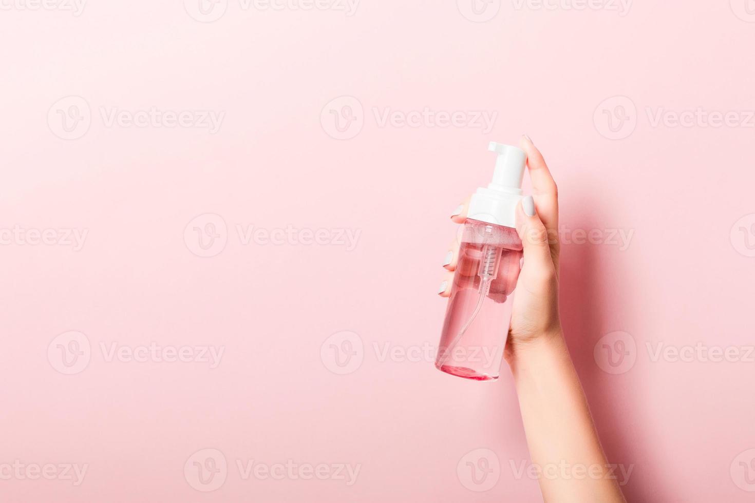 femelle main en portant vaporisateur crème bouteille de lotion isolé. fille donner cosmétique des produits sur rose Contexte photo