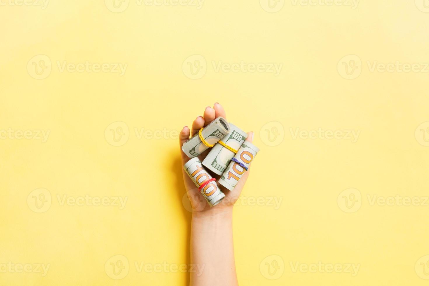 Haut vue de roulé en haut dans tubes dollar factures dans femelle paume sur coloré Contexte. la pauvreté et dette concept photo